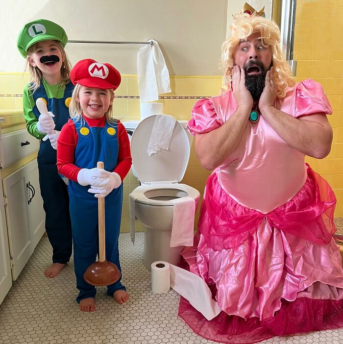 Dad and daughters in funny costumes, dressed as video game characters in a bathroom setting, looking adorable.