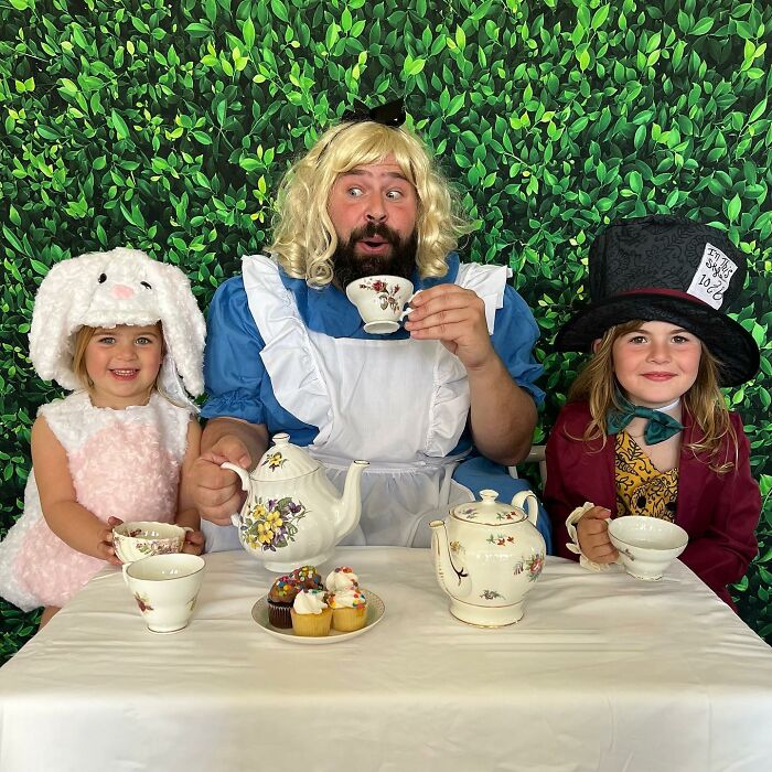 Dad and daughters in funny costumes having a tea party with cupcakes, featuring whimsical outfits.