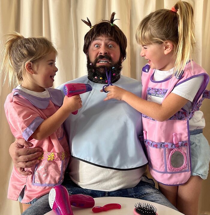 Dad playfully poses with daughters in costumes, creating funny and adorable moments together.