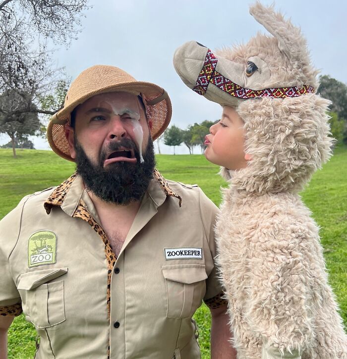 Dad making funny face with daughter in llama costume, outdoors.