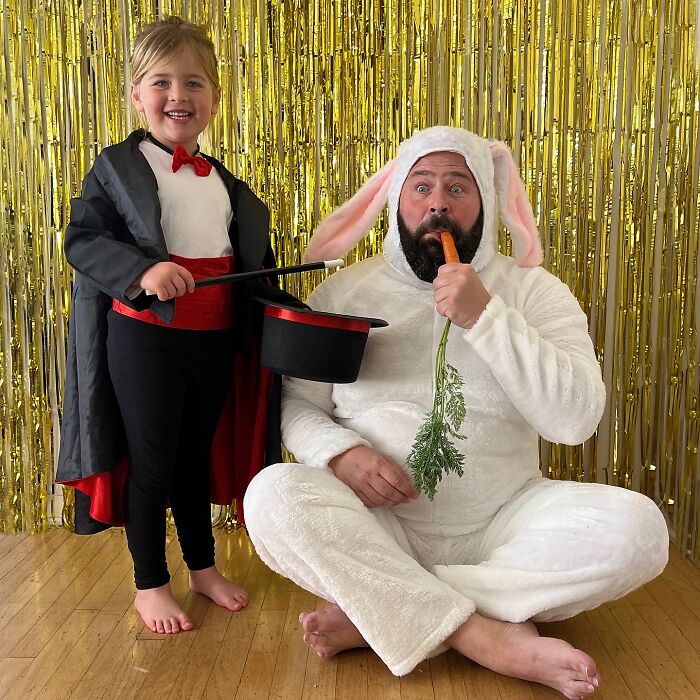 Dad in bunny costume with daughter dressed as magician, holding a hat; fun and adorable family moment.