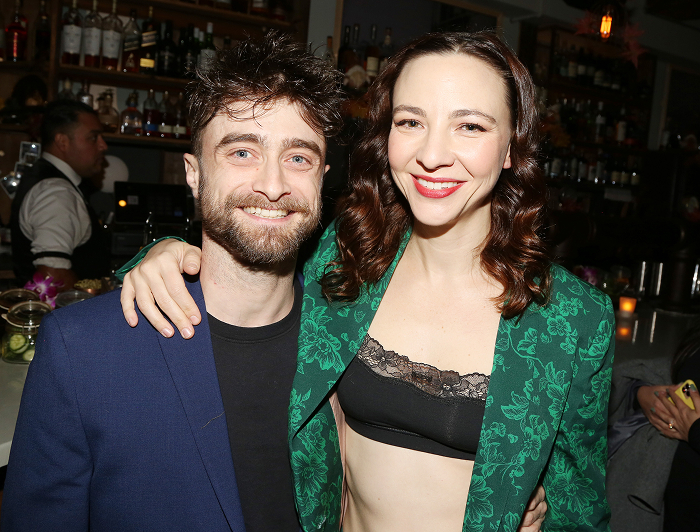 Daniel Radcliffe and Erin Darke smiling together in a lively bar setting.
