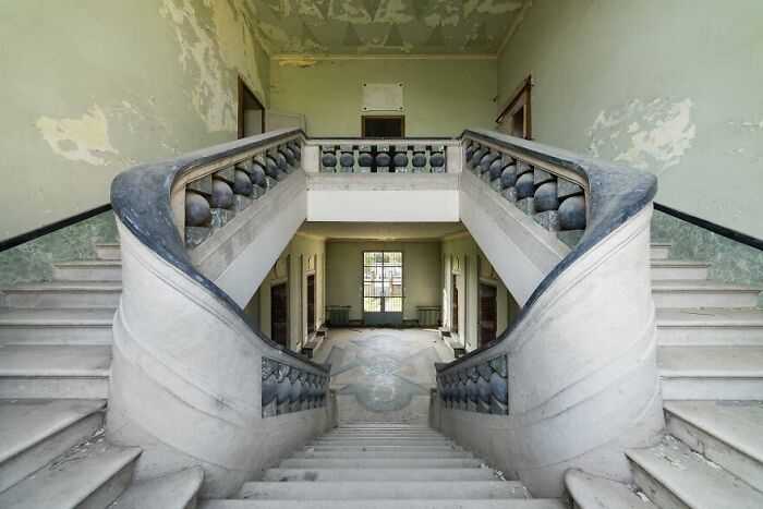 Abandoned grand staircase in a decaying building, showcasing architectural beauty over time.