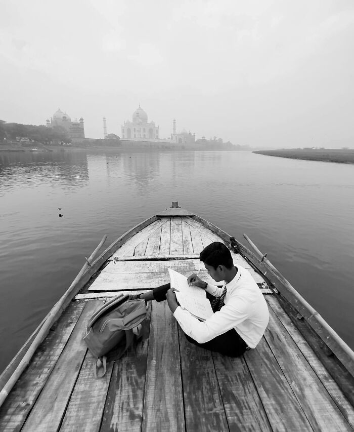 Black and white photo of a person reading on a boat with the Taj Mahal in the background, capturing a serene split-second moment.