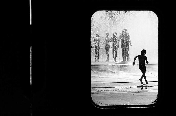 Child running near fountain, silhouetted in a black and white photograph, capturing split-second moments.