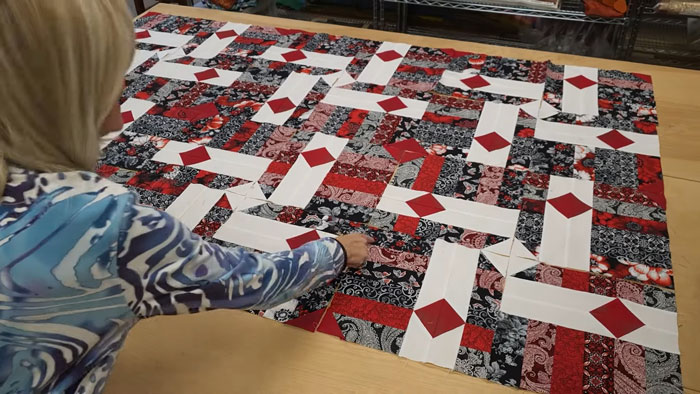 Person arranging a colorful patchwork quilt on a table, focusing on quilting patterns in a cozy workspace.