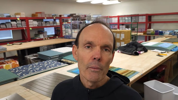 Man in a workshop setting shares news about beloved YouTuber's passing.