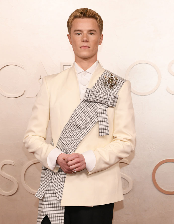 Person in a unique white suit with a checkered sash at Oscars 2025, showcasing fashionably challenged looks.