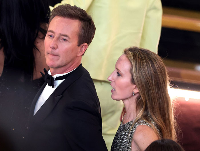 Man and woman at awards ceremony, wearing formal attire, amidst lively crowd, capturing reactions to Oscar results.