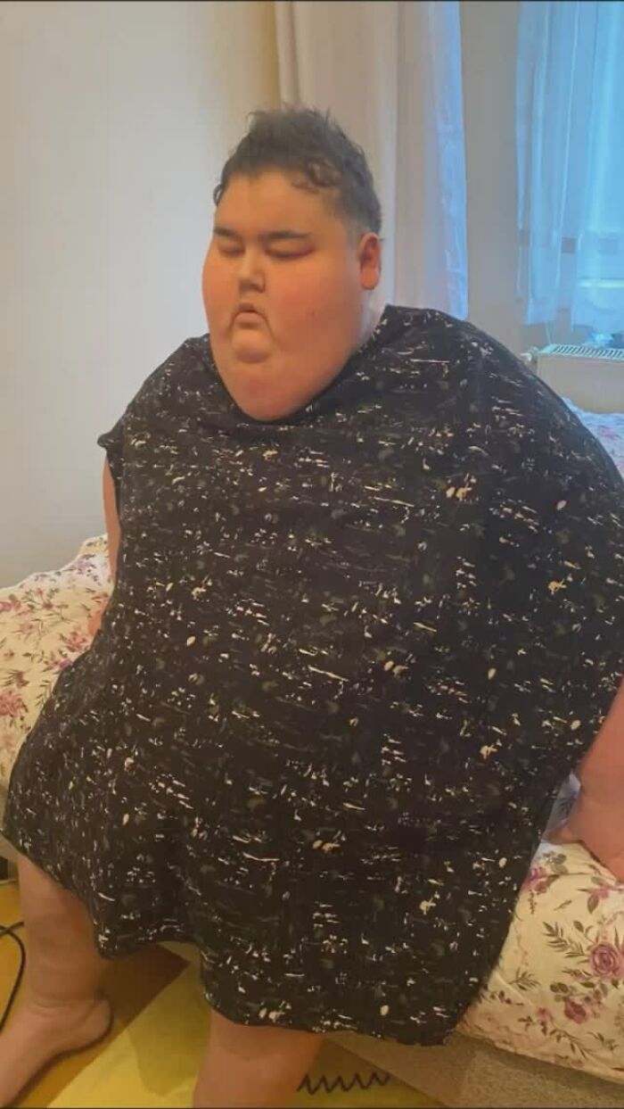 Person sitting in a room, associated with viral "Mukbang" videos, wearing a patterned shirt. Person sitting in a room, associated with viral "Mukbang" videos, wearing a patterned shirt.