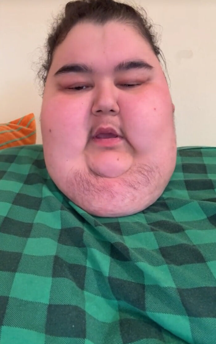 A person known for viral mukbang videos in a checkered shirt, sitting on an orange cushion. A person known for viral mukbang videos in a checkered shirt, sitting on an orange cushion.