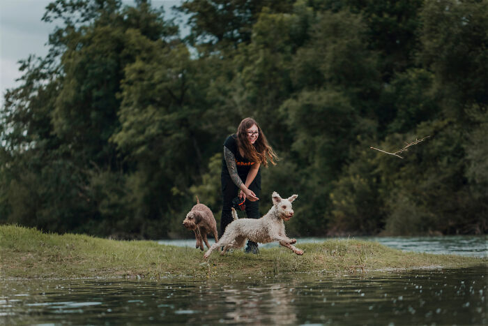 Woman playing fetch with two dogs by a river, showcasing a special bond between animals and their humans.