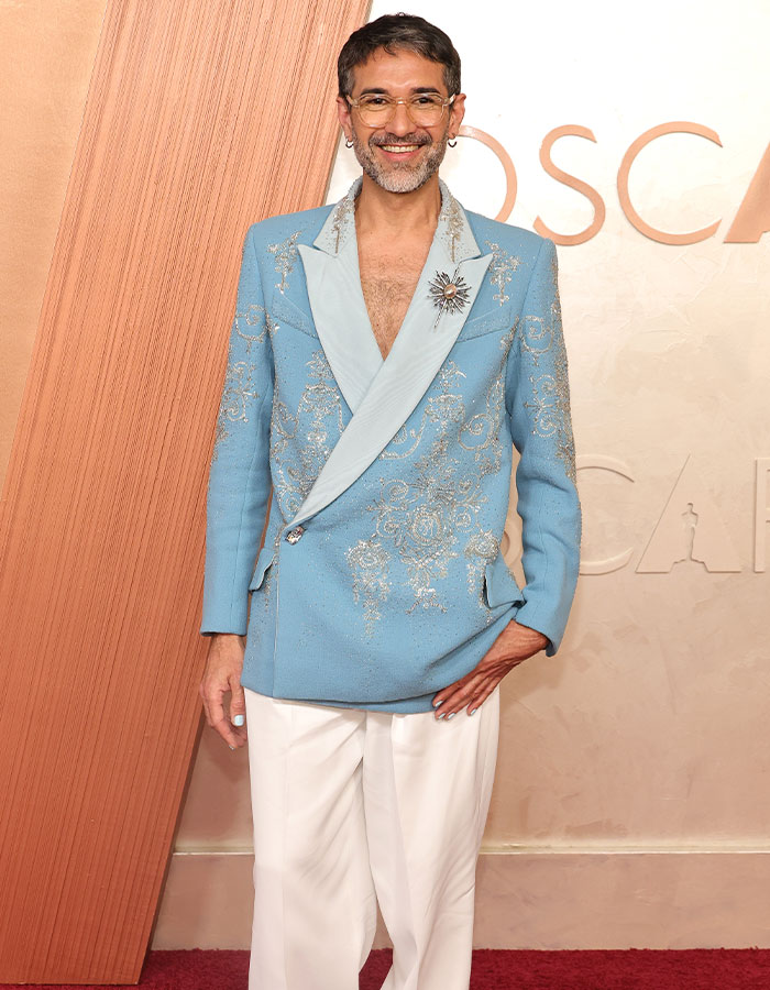 Person in a bold blue embroidered blazer and white pants on the Oscars 2025 red carpet.