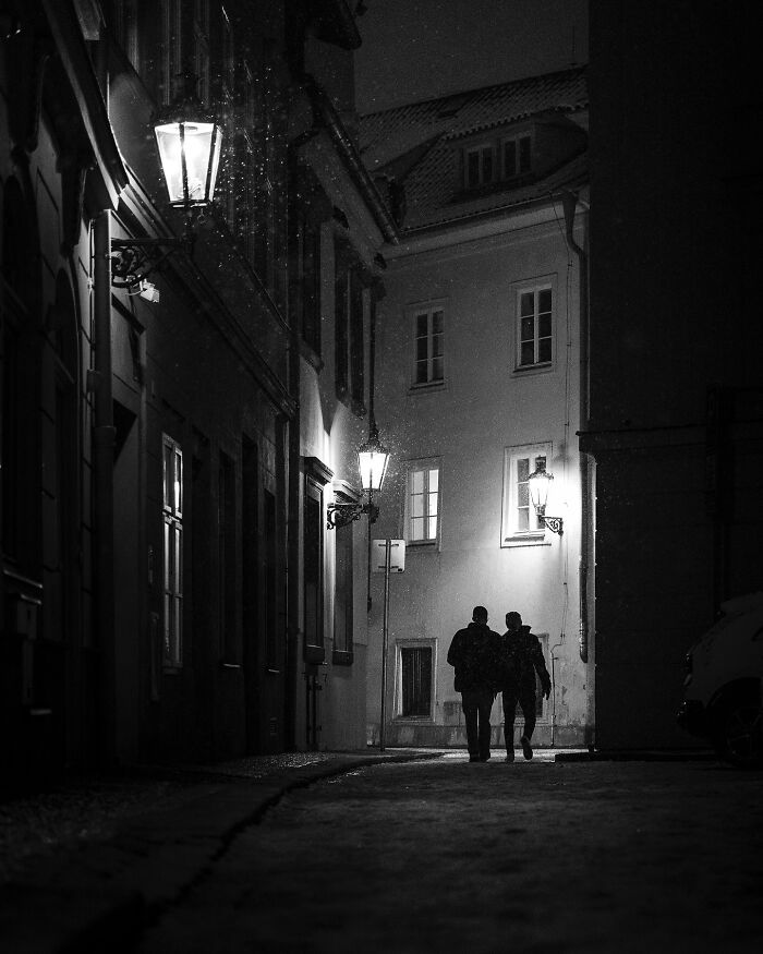 Two figures walking down a dimly lit street at night, captured in black-and-white street photography.