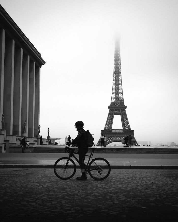 Black-and-white street photograph of a cyclist near the Eiffel Tower.