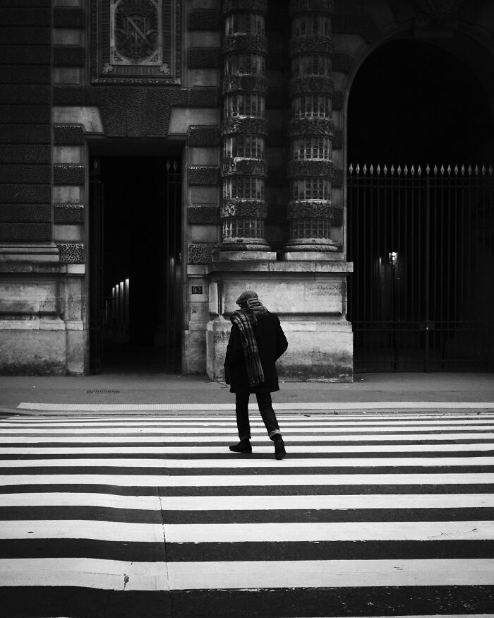 A lone figure crossing a zebra line in a black-and-white street photograph, capturing urban life.