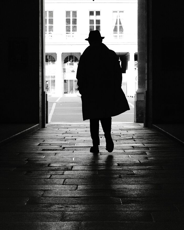 Silhouette of a person in a hat and coat walking through a tunnel in black-and-white street photography.