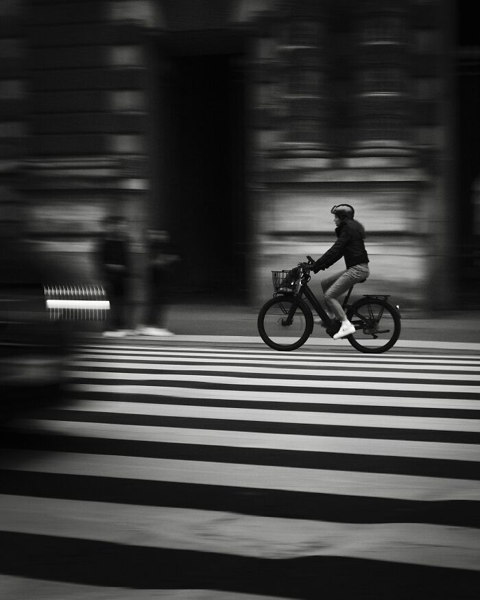 Biker crossing street in a black-and-white photograph, capturing motion and urban life.