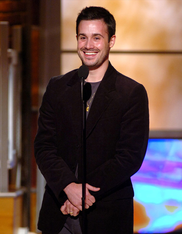 Smiling nepo baby in a black suit on stage with a microphone, showcasing talent in an event setting.