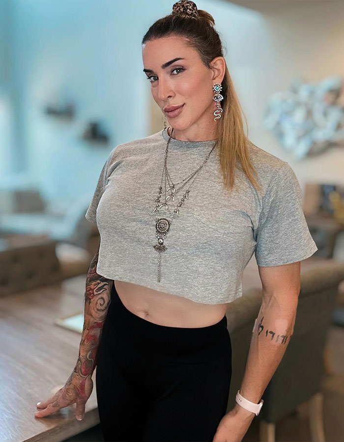 Former WWE star in a grey crop top and earrings, showing her transition journey with confidence in a bright room.