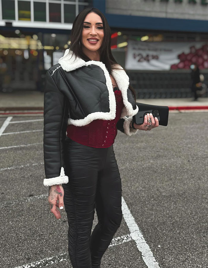 Former WWE star in a black jacket and burgundy corset, smiling in a parking lot, showcasing transition.