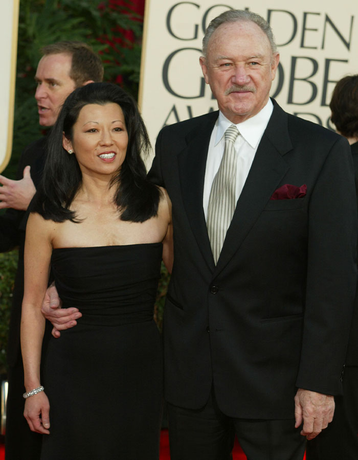 Gene Hackman at an event with a woman in a black dress, standing on a red carpet. Gene Hackman at an event with a woman in a black dress, standing on a red carpet.