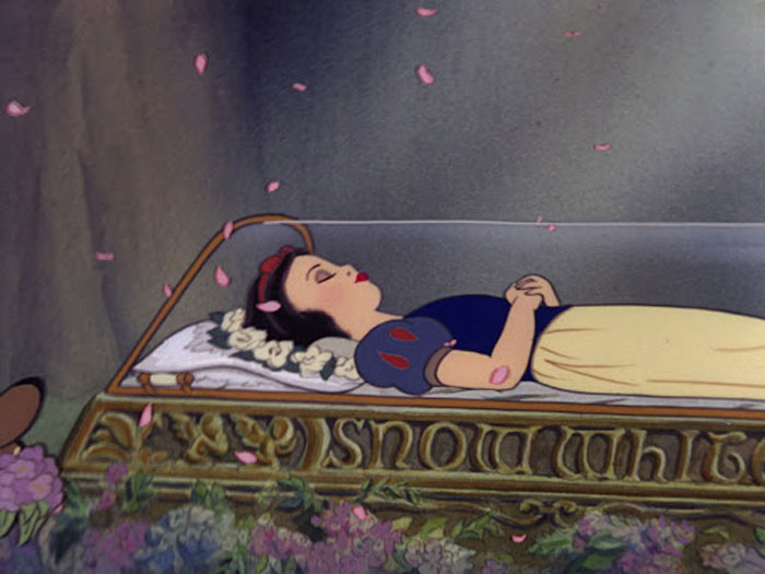Snow White in a glass coffin surrounded by flowers and falling petals in the remake scene.