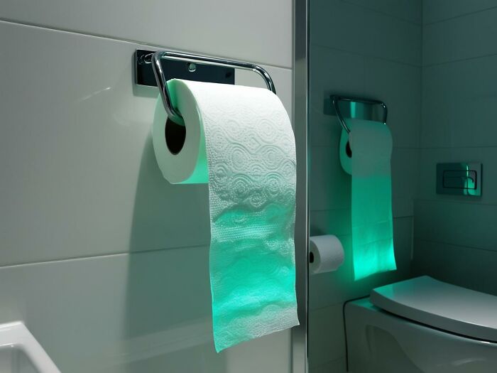 Illuminated toilet paper roll with a green glow, mounted on a wall in a modern bathroom setting.