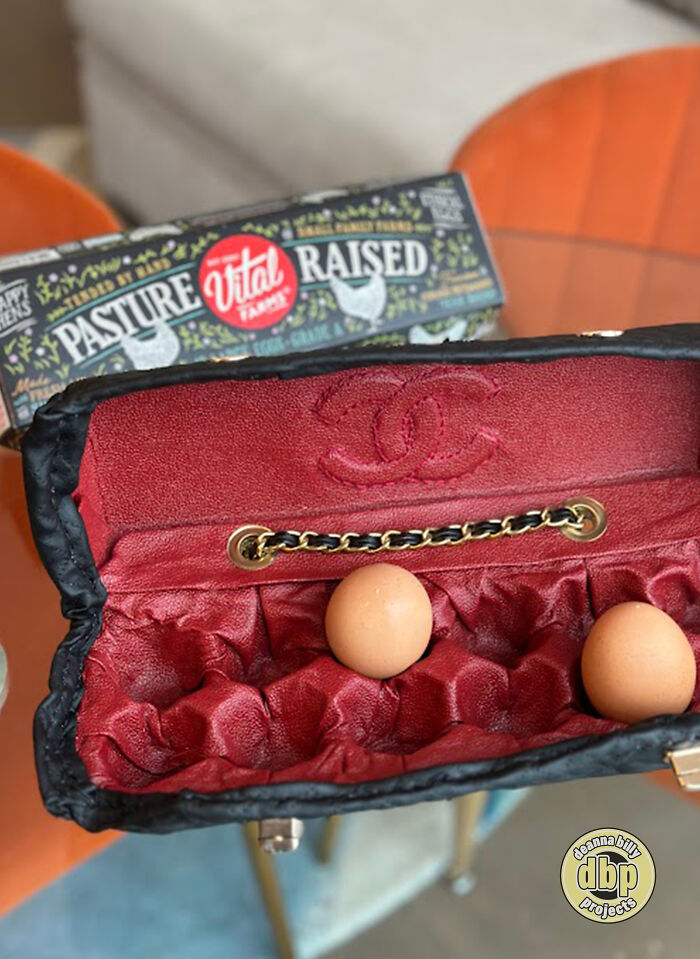 Luxury handbag carrying eggs as a commentary on high prices, with a carton of pasture-raised eggs in the background. Luxury handbag carrying eggs as a commentary on high prices, with a carton of pasture-raised eggs in the background.