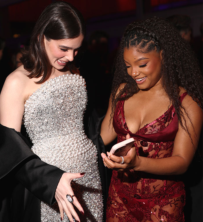 Two women in elegant gowns sharing a moment at Oscars 2025, one holding a phone, smiling warmly.