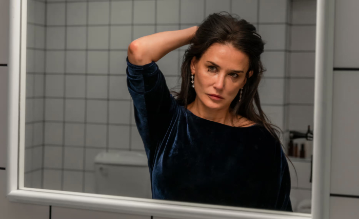 Woman in blue dress with pensive expression looking at herself in a bathroom mirror. Woman in blue dress with pensive expression looking at herself in a bathroom mirror.