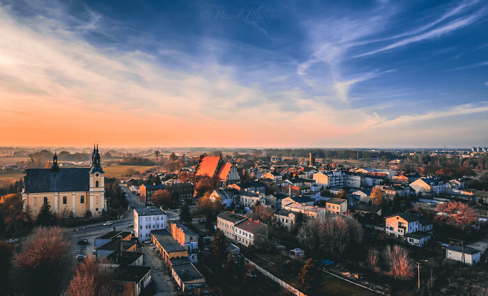 Aerial view of a city during sunset with a prominent church and houses scattered around, illustrating the city's landscape.