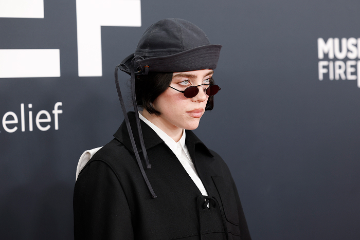 Billie Eilish in a black hat and sunglasses at a public event, sparking dating rumors and speculation about her silence.