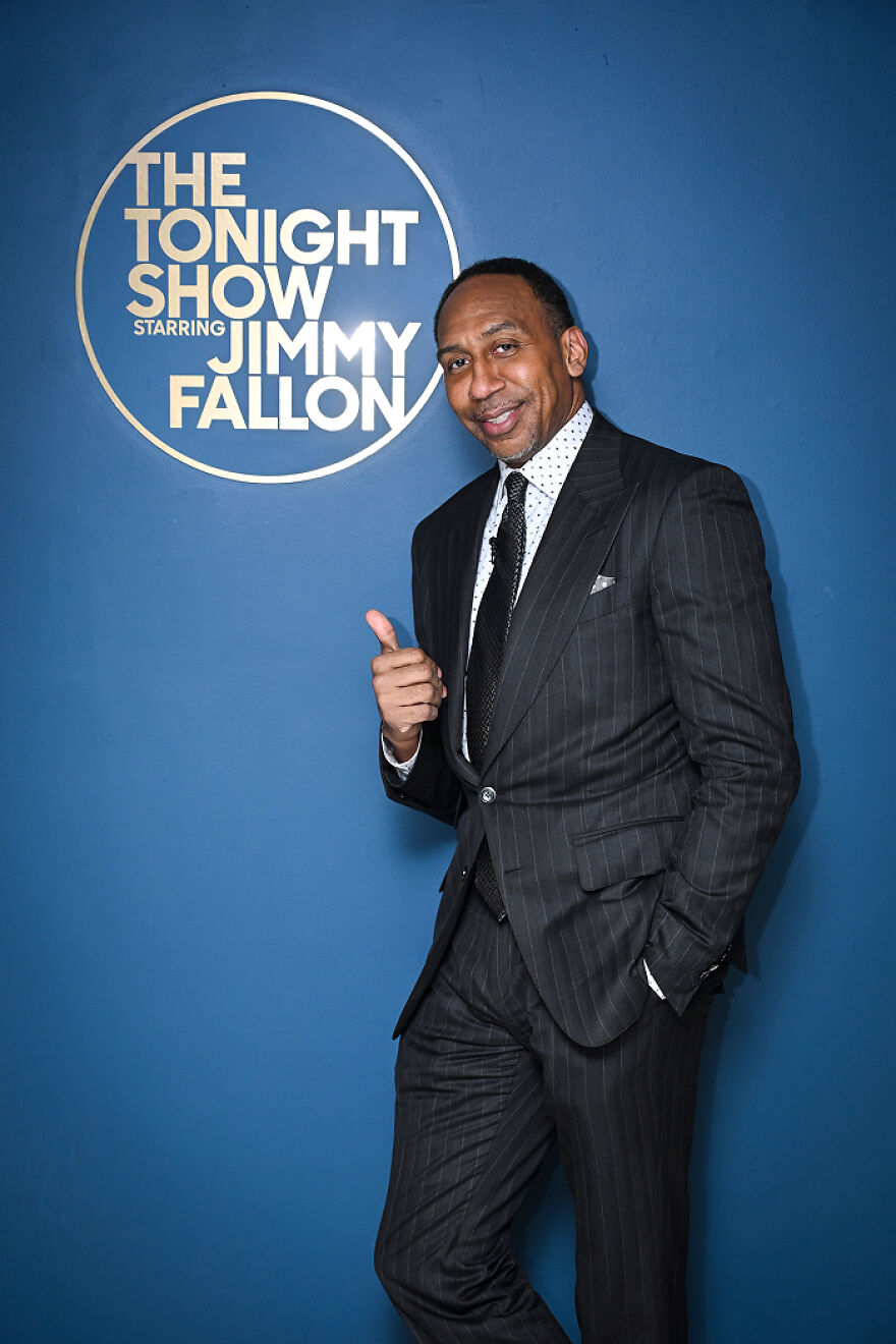 Stephen A. Smith in a pinstripe suit posing with a thumbs up in front of "The Tonight Show" logo.