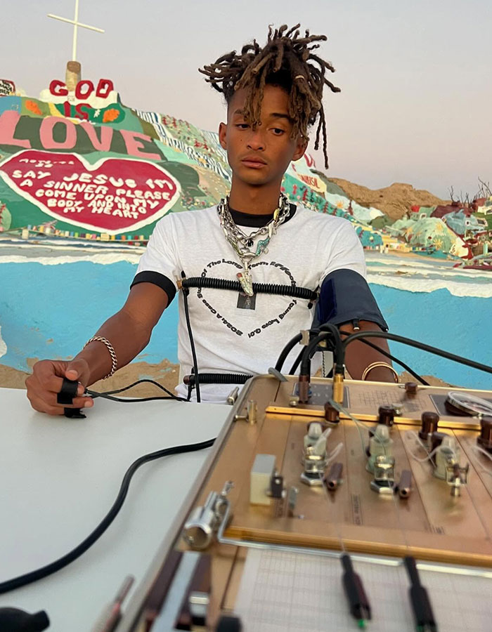 Person with unusual style at colorful location, seated with equipment. Sparks concern for 'strange' appearance.