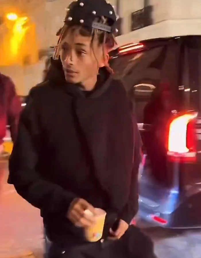 Jaden Smith with unique style, holding a drink near a car at night.