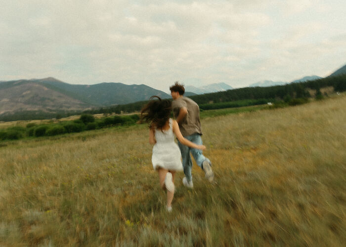 Couple running through a meadow, highlighting the best engagement photos of 2025 with scenic mountain views.