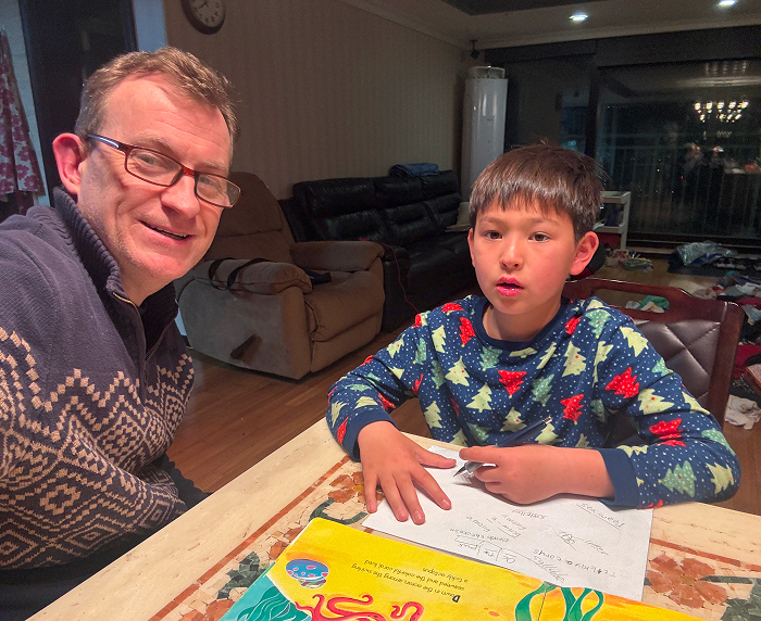 Man in glasses and a festive sweater with his son doing homework, reminiscent of viral "BBC Dad" moment. Man in glasses and a festive sweater with his son doing homework, reminiscent of viral "BBC Dad" moment.