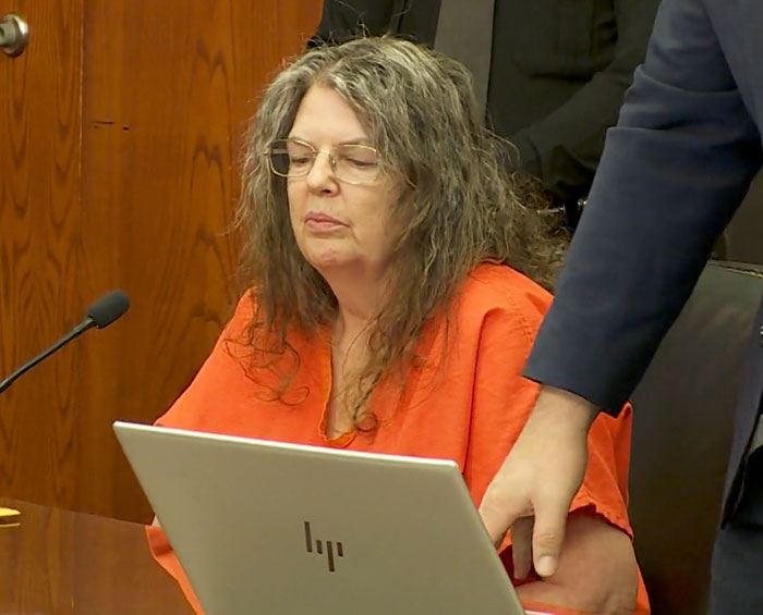 Person in an orange jumpsuit seated at a courtroom table during a legal proceeding. Person in an orange jumpsuit seated at a courtroom table during a legal proceeding.