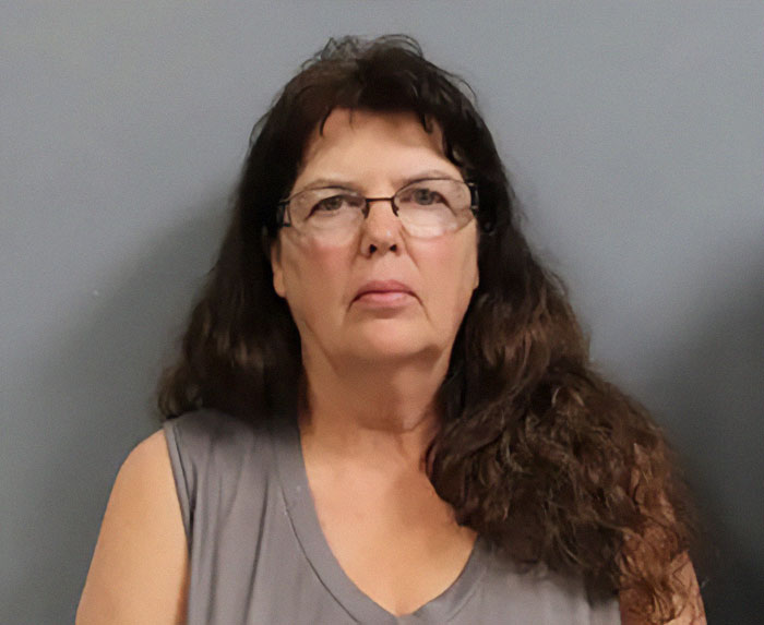 Female suspect in a legal case involving adopted children, wearing glasses and a grey shirt, against a plain background. Female suspect in a legal case involving adopted children, wearing glasses and a grey shirt, against a plain background.