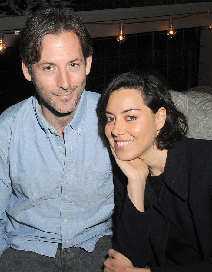 A couple sitting together at an outdoor event, smiling at the camera, with string lights in the background.