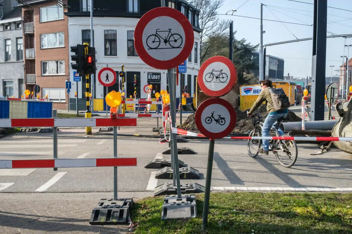Cyclist passes multiple bicycle signs amidst construction, capturing the absurd human condition.