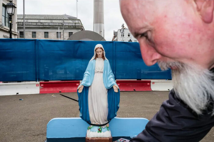 Belgian photographer captures absurd human condition with a statue of the Virgin Mary and a man's face in an urban setting.