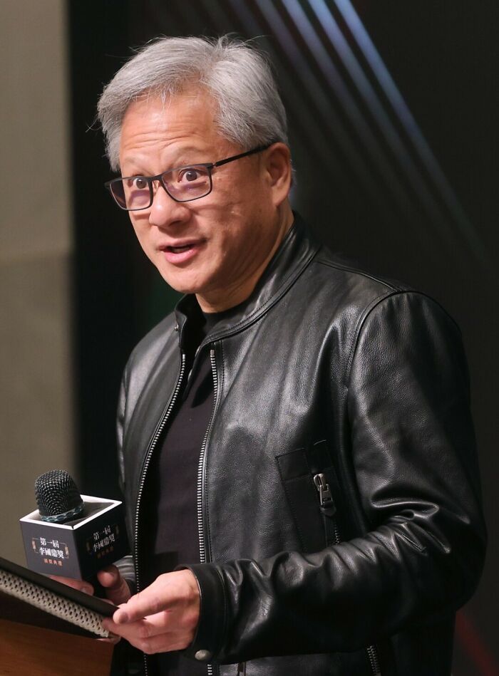 Man wearing glasses and a black leather jacket speaking at a podium about the richest people and global wealth disparity.