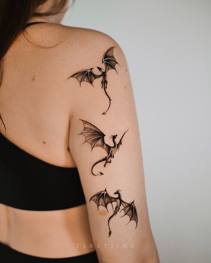 Woman with fine-line tattoos of three small dragons on her shoulder and arm.