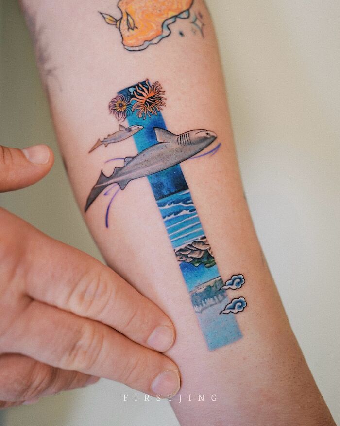 Fine-line tattoo featuring dreamy ocean setting with sharks and flowers on an arm.