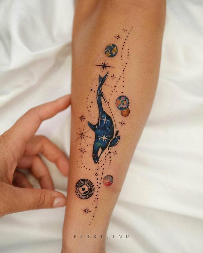 Fine-line tattoo of an orca and planets on an arm, creating a dreamy setting.