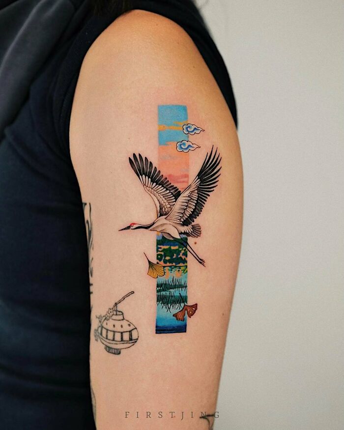 Fine-line tattoo featuring a crane and dreamy landscape on upper arm.
