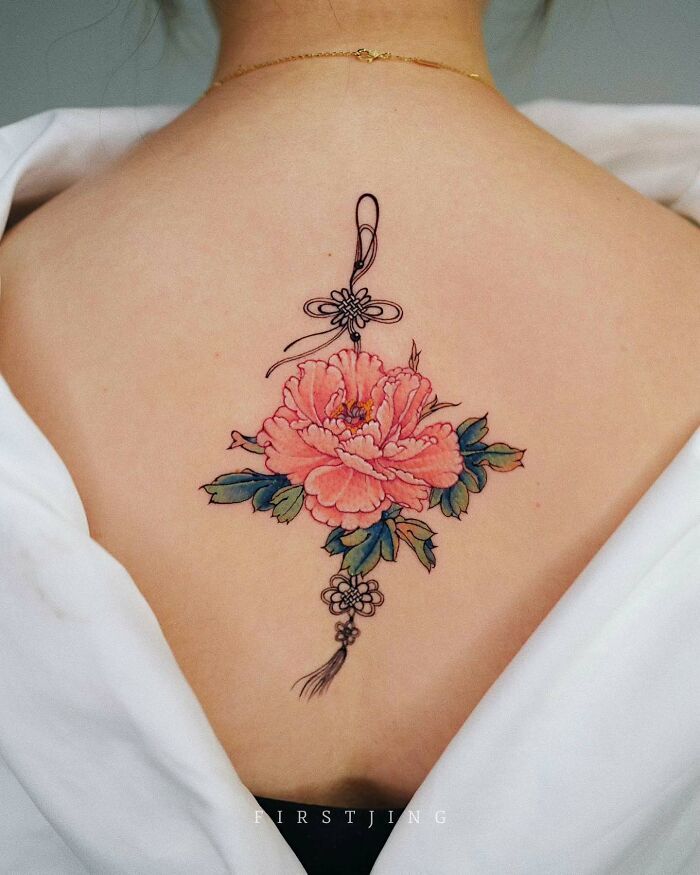 Fine-line tattoo of a pink peony flower with a decorative design on a woman's upper back.