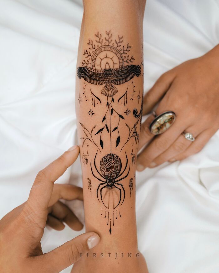 Fine-line tattoo on forearm with intricate, dreamy design featuring bird, leaves, and a stylized spider motif.
